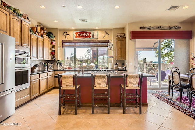 kitchen featuring visible vents, a kitchen bar, stainless steel appliances, dark countertops, and a healthy amount of sunlight