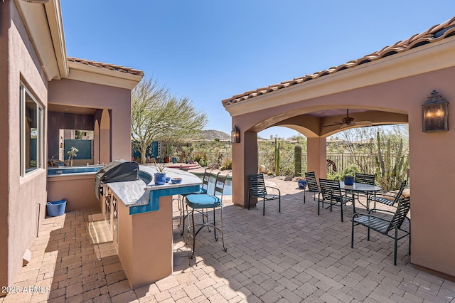 view of patio / terrace with fence, a swimming pool, ceiling fan, outdoor dining space, and outdoor dry bar