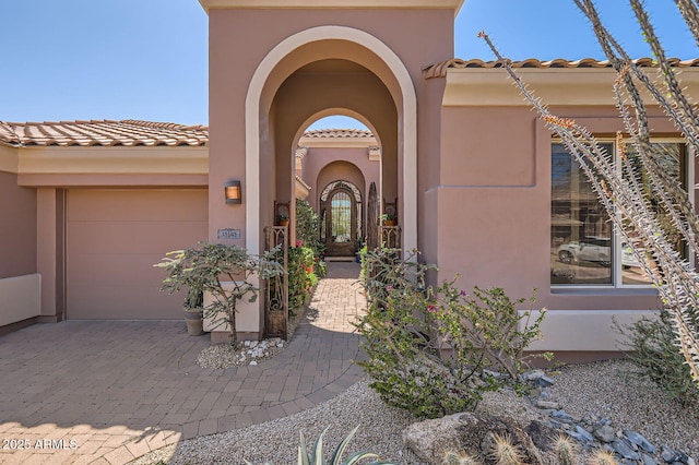 entrance to property featuring a tile roof, decorative driveway, a garage, and stucco siding