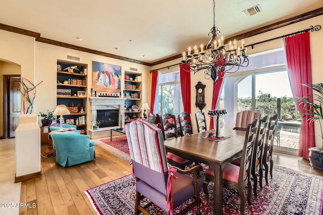 dining space featuring light wood-type flooring, ornamental molding, a chandelier, visible vents, and a glass covered fireplace
