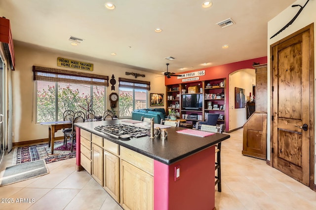 kitchen featuring stainless steel gas stovetop, visible vents, dark countertops, a kitchen island, and arched walkways