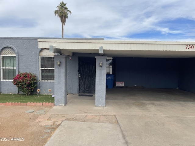 view of exterior entry with concrete driveway, a carport, and stucco siding