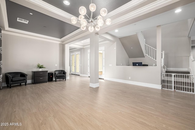living area with wood finished floors, an inviting chandelier, a tray ceiling, ornamental molding, and stairs