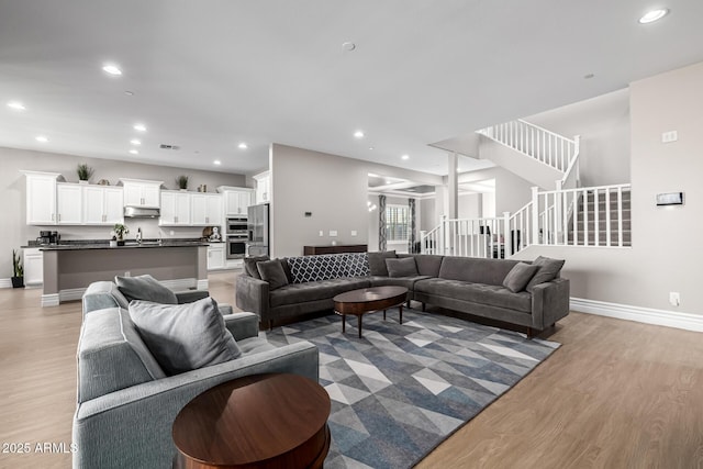 living room featuring stairway, recessed lighting, light wood-type flooring, and baseboards