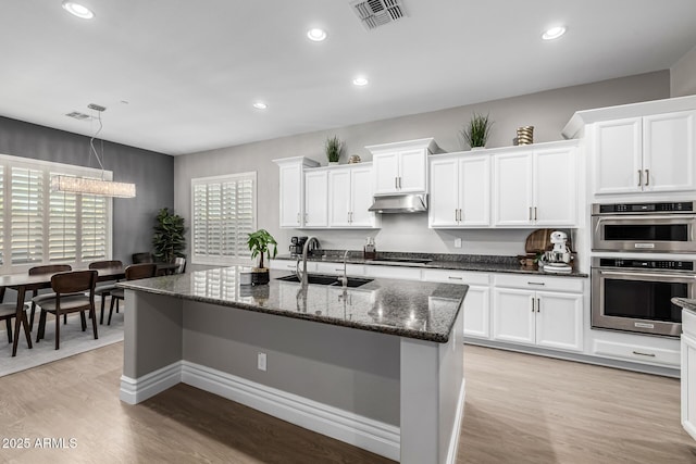 kitchen with under cabinet range hood, visible vents, light wood-style floors, and a sink