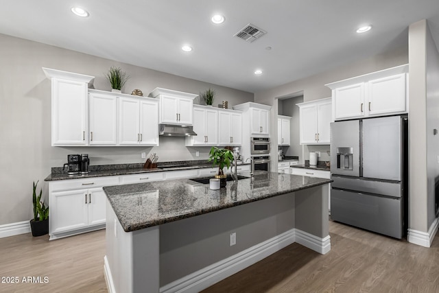 kitchen with visible vents, under cabinet range hood, dark stone countertops, stainless steel appliances, and white cabinetry