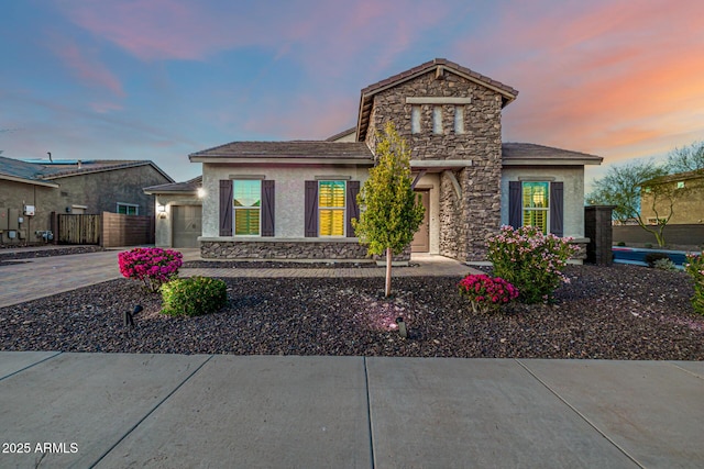 view of front of property with an attached garage, fence, stucco siding, stone siding, and driveway