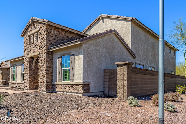 view of property exterior with stucco siding, stone siding, and fence