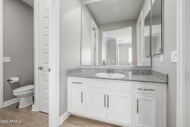 bathroom featuring vanity, toilet, wood finished floors, and baseboards