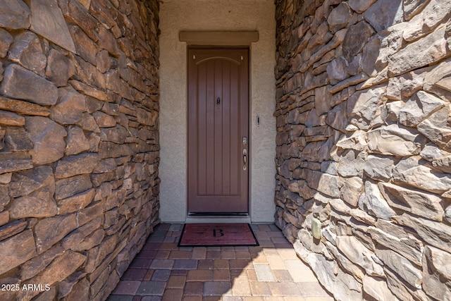 doorway to property featuring stone siding and stucco siding