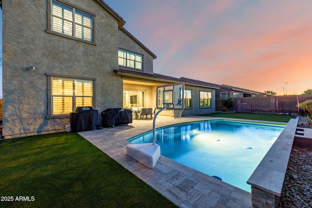pool at dusk with grilling area, a fenced in pool, fence, a yard, and a patio
