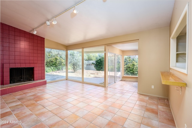 unfurnished sunroom featuring rail lighting, vaulted ceiling, and a tile fireplace