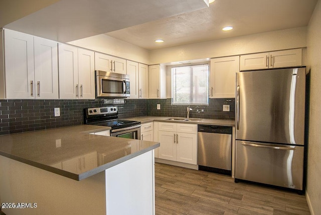 kitchen featuring sink, kitchen peninsula, hardwood / wood-style flooring, stainless steel appliances, and white cabinets