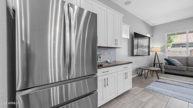 kitchen featuring dark stone countertops, tasteful backsplash, freestanding refrigerator, white cabinets, and baseboards
