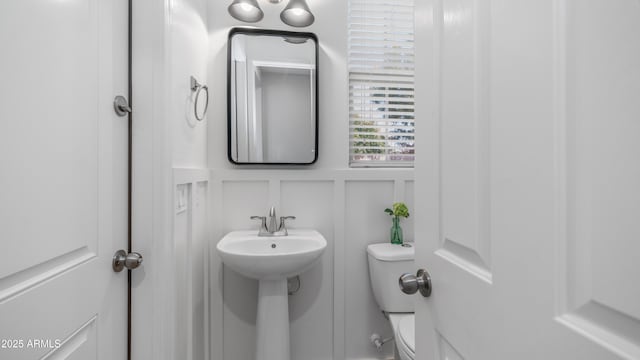 half bath with toilet, a sink, and a decorative wall