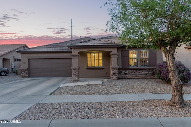 view of front of house featuring a tiled roof, concrete driveway, stucco siding, stone siding, and a garage