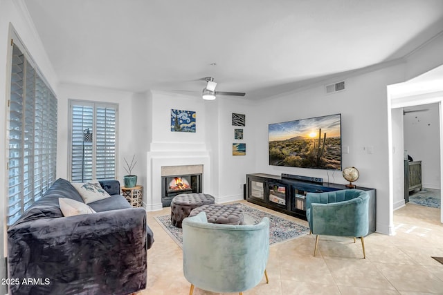 living area featuring a glass covered fireplace, ceiling fan, ornamental molding, and visible vents