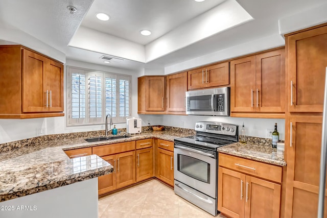 kitchen with a sink, brown cabinetry, stainless steel appliances, and a tray ceiling