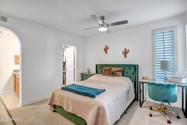 bedroom with light carpet, a walk in closet, connected bathroom, arched walkways, and a ceiling fan