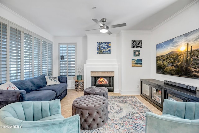 living room featuring crown molding, a ceiling fan, baseboards, and a warm lit fireplace