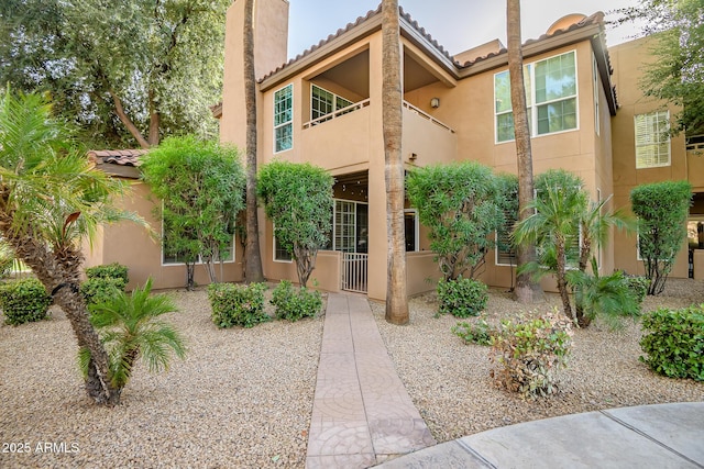 view of front of house with a balcony, a chimney, a tile roof, and stucco siding