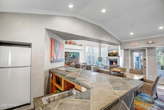 kitchen with a warm lit fireplace, a sink, freestanding refrigerator, recessed lighting, and lofted ceiling