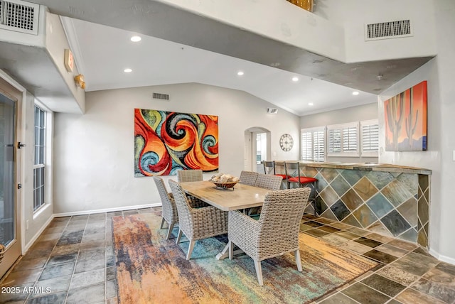 dining room featuring visible vents, stone tile flooring, lofted ceiling, baseboards, and arched walkways