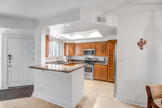 kitchen with appliances with stainless steel finishes, brown cabinetry, dark stone counters, a peninsula, and visible vents