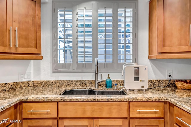 interior details featuring a sink, a textured wall, light stone countertops, and brown cabinets