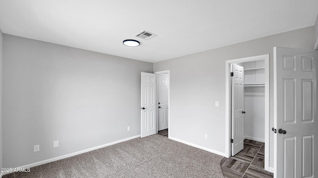 unfurnished bedroom with dark carpet, baseboards, a spacious closet, visible vents, and a closet