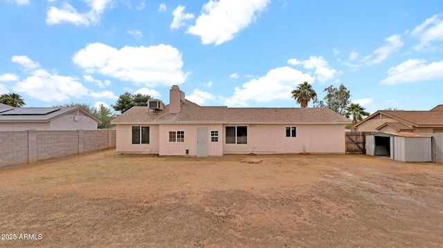 rear view of house featuring central AC, an outbuilding, a chimney, and a fenced backyard