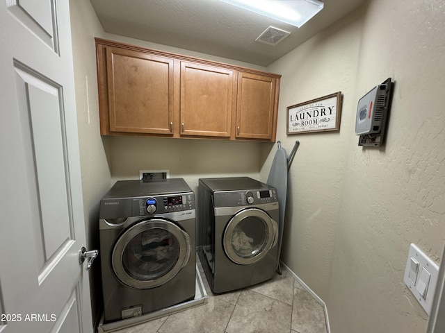 clothes washing area featuring cabinets, light tile patterned floors, and washing machine and clothes dryer