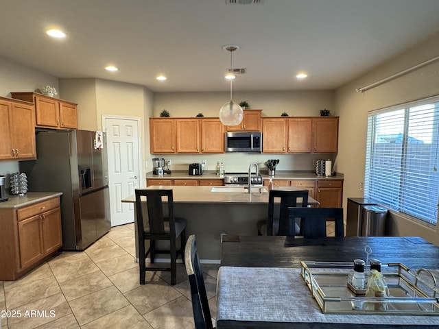 kitchen featuring pendant lighting, light tile patterned floors, sink, stainless steel appliances, and an island with sink