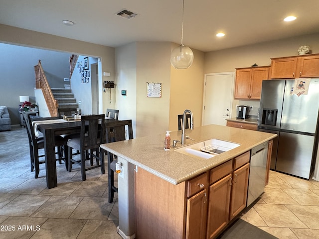 kitchen featuring sink, stainless steel appliances, an island with sink, light tile patterned flooring, and decorative light fixtures