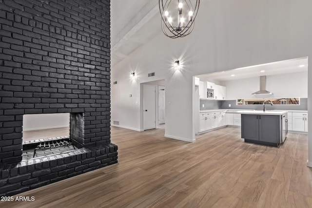 interior space featuring sink, a chandelier, a brick fireplace, light wood-type flooring, and a towering ceiling