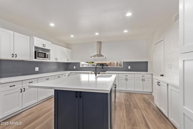 kitchen with a kitchen island with sink, wall chimney range hood, white cabinetry, and sink