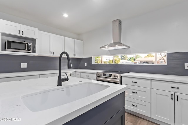 kitchen with sink, appliances with stainless steel finishes, white cabinets, wall chimney range hood, and backsplash