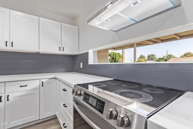 kitchen with stainless steel electric range, exhaust hood, decorative backsplash, and white cabinets