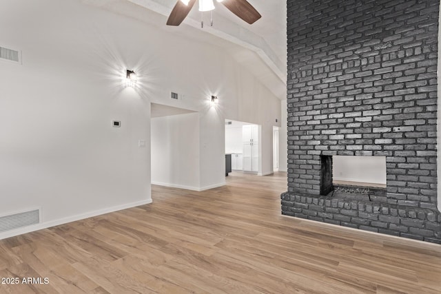 unfurnished living room featuring ceiling fan, a fireplace, high vaulted ceiling, and light hardwood / wood-style flooring