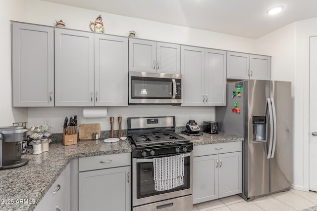 kitchen with light tile patterned floors, light stone counters, appliances with stainless steel finishes, and gray cabinets