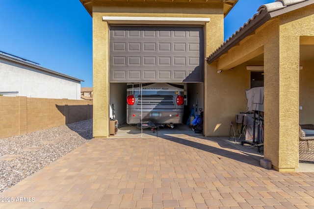 view of car parking with decorative driveway, a garage, and fence