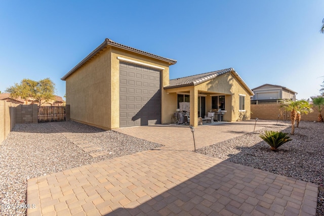 rear view of property featuring a tiled roof, stucco siding, fence, and a gate