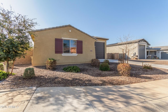 view of front of house featuring fence, a tiled roof, stucco siding, a garage, and driveway