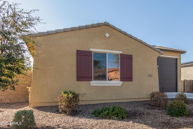 view of side of home featuring a tiled roof, an attached garage, fence, and stucco siding