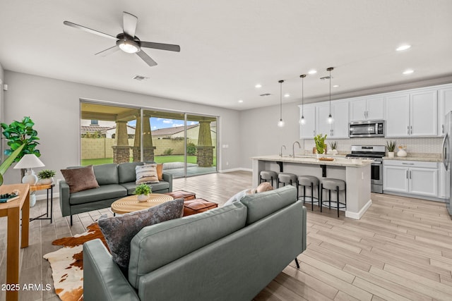 living room featuring recessed lighting, light wood finished floors, a ceiling fan, and baseboards