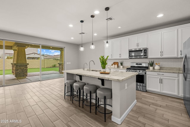 kitchen featuring stainless steel appliances, a kitchen island with sink, light wood-style floors, white cabinetry, and decorative backsplash