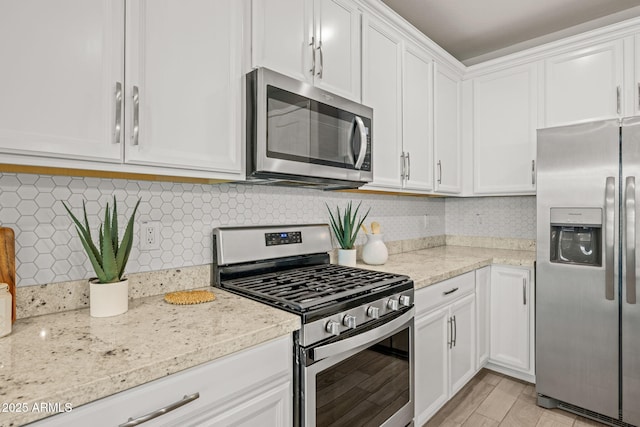 kitchen with stainless steel appliances, white cabinetry, light stone countertops, and backsplash