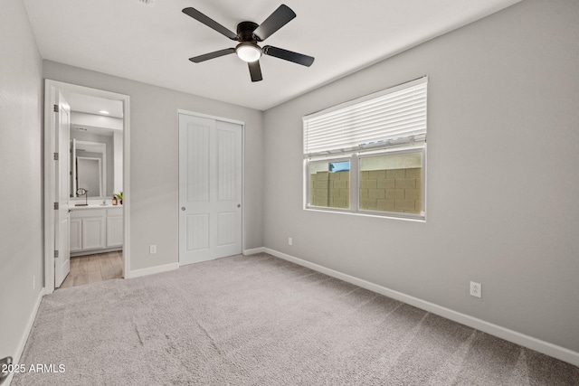 unfurnished bedroom with light carpet, baseboards, ensuite bathroom, a closet, and ceiling fan