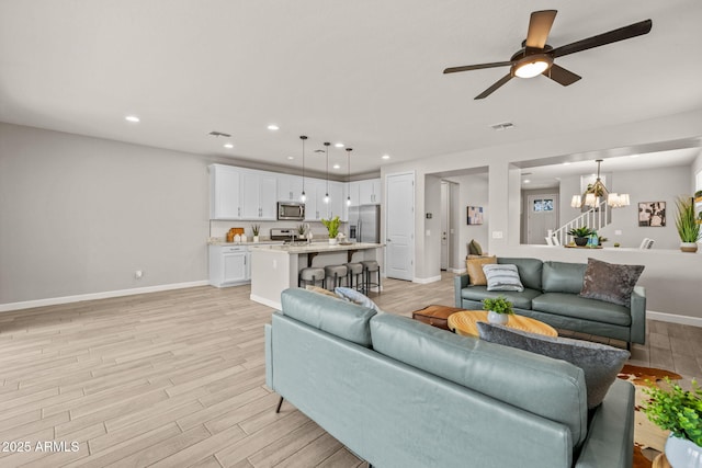 living area featuring light wood-style floors, recessed lighting, ceiling fan, baseboards, and a chandelier