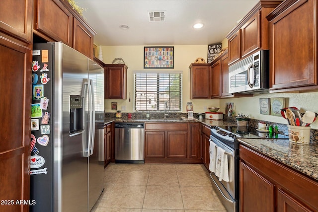 kitchen with visible vents, dark stone counters, a sink, light tile patterned floors, and stainless steel appliances